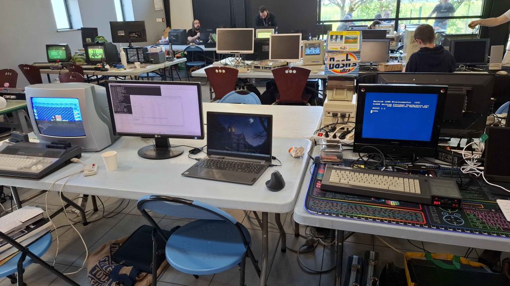 CrocoFest 2026 : Alignement d'ordinateurs vintage Amstrad et Enterprise 128 sur des tables de camping lors du festival rétro CrocoFest en bord de rivière.